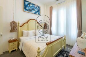 Bedroom with cream bed, abstract blue artwork and rattan pendant lamps at Villa Jendari